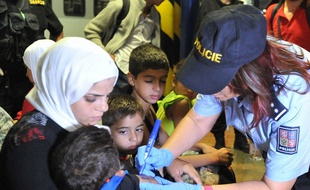 Une policière tchèque en train d'inscrire au marqueur un numéro d'identification sur le bras d'un enfant réfugié syrien.