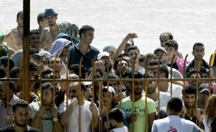 Des migrants attendent derrière une barrière pour entrer dans le stade de l'ïle de Koos pour se faire enregistrer administrativement, le 12 août 2015