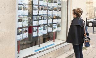 Une femme consulte les annonces immobilières devant une agence à Bordeaux.
